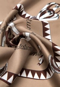 Tessuto marrone setoso con un motivo vorticoso che presenta accenti crema e marrone scuro, incluso un design geometrico e elementi di testo.