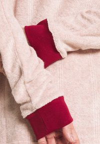 Light pink long-sleeve top with terry cloth texture and red ribbed cuffs. The sleeves show subtle stitching details along the seams.