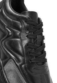 Scarpa sportiva nera realizzata con pelle liscia e suede texturizzato, dotata di punta tonda, lacci piatti e dettagli di cucitura discreti.
