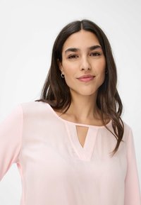 Helles pinkes Blusenshirt mit einem Keyhole-Ausschnitt, gefertigt aus einem glatten Stoff. Sie verfügt über lange Ärmel und eine lockere Passform.