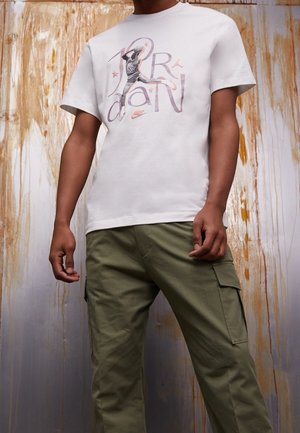 Short-sleeve white jersey t-shirt with a printed graphic of a basketball player and stylized text, paired with olive green cargo pants.