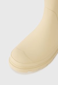 Botte de cheville en caoutchouc beige clair avec une finition lisse, un bout rond et une semelle texturée. Design simple sans quincaillerie ni motifs visibles.