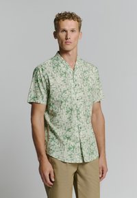 Korte mouwen shirt in lichtgroen met een geometrische print in donkerder groen, voorzien van een kraag en knoopsluiting.