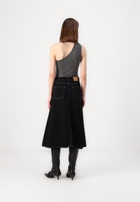 Svart ankellang skirt med hvite sømmer, kombinert med en stripe-frontend topp. Beina dekket av elegante svarte knelange støvler.