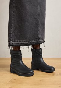 Boots de gleznă din piele neagră, cu un design căzut, talpi groase și fermoare laterale, asociate cu o fustă din denim negru destrămată.