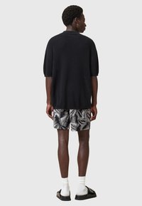 Maglione nero a maglia oversize a maniche corte abbinato a pantaloni corti a fantasia bianco e nero, indossato con calze bianche e sandali neri.