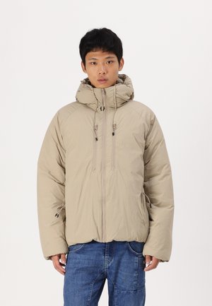 Beige padded jacket with a high collar, two front zippers, and elastic cuffs. Features a smooth texture and drawstrings at the hood. Blue denim jeans.