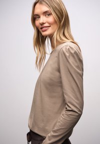 Beiges langärmeliges Oberteil mit rundem Ausschnitt; verfügt über geraffte Details an den Schultern; weiche Textur, figurbetontes Design.