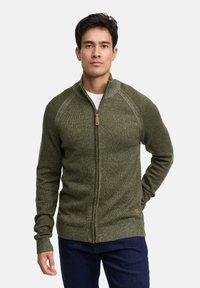 Gebreide groene trui met rits en hoge kraag, voorzien van raglanmouwen en geribde boorden, afgewerkt met een tankleurige ritstrekker en een subtiele textuur.