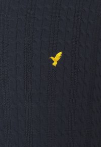 Tissu tricoté bleu foncé avec un petit emblème d'oiseau jaune brodé au centre.