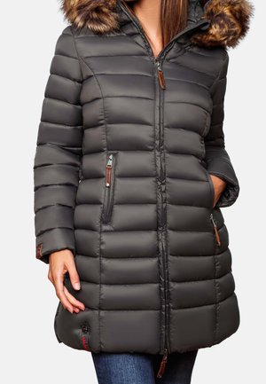 Woman wearing a knee-length, dark gray quilted winter coat with fur-trimmed hood and zipper pockets, hands partially in pockets.