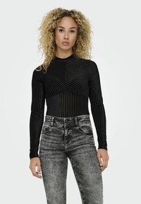 Body nero a maniche lunghe con texture a righe verticali; design aderente con collo alto. Indossato con jeans neri in denim a vita alta.