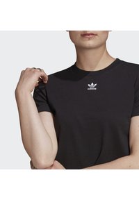 Svart bomull t-shirt med korta ärmar, med en vit broderad Adidas-logotyp på bröstet. Slät textur och klassisk passform.