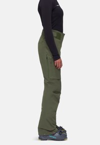 Gröna vattentäta skidbyxor med hög midja, sidoklappar och smal passform, kombinerat med svarta skidboots med gula accenter.