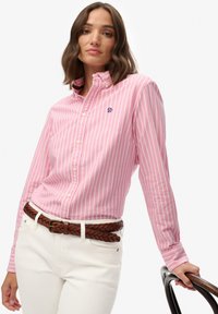 Camicia a righe rosa chiaro con colletto, caratterizzata da righe bianche e rosa scuro, abbinata a pantaloni bianchi e una cintura intrecciata marrone.