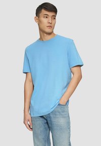 Svetlomodré bavlnené tričko s okrúhlym výstrihom a krátkymi rukávmi, ktoré má voľný strih a hladkú textúru. V kombinácii s svetlými džínsami.