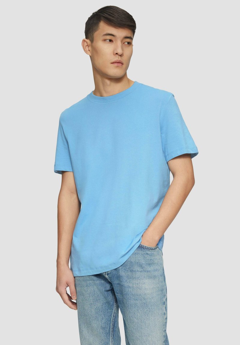 Svetlomodré bavlnené tričko s okrúhlym výstrihom a krátkymi rukávmi, ktoré má voľný strih a hladkú textúru. V kombinácii s svetlými džínsami.