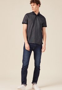 Polo navy a maniche corte, in tessuto testurizzato, con patta a tre bottoni, abbinato a jeans blu scuro e sneakers bianche.