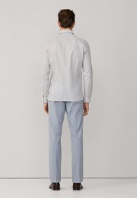 Gestreiftes Hemd in Weiß und Hellblau, mit langen Ärmeln, taillierter Passform und spitzem Kragen, kombiniert mit hellblauen Hosen und braunen Schuhen.