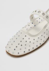 White fabric shoe with a flat design, adorned with silver rhinestones, featuring a round toe and a single strap across the instep.