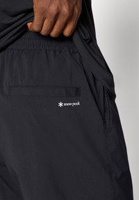Black shorts made of lightweight fabric featuring an elastic waistband, side pockets, and a rear pocket with a white "snow peak" logo.