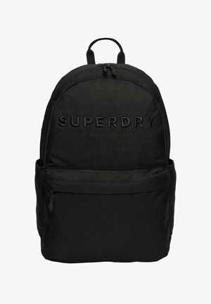 Mochila de tela negra con el logo "SUPERDRY" en relieve, forma redondeada, un compartimento principal y un bolsillo frontal con cremallera. Tiras ajustables y acolchadas.