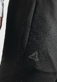 Schwarzer wasserdichter Stoff mit strukturierten Oberflächen, versehen mit Tropfen und einem dezenten Logo-Detail in der unteren Ecke.