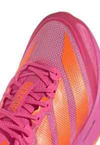 Roosa spordijalats oranžide triipude ja paeltega, võrkmaterjalist pealne ning "ADIZERO" ja "LIGHTSTRIKE PRO" brändinguga.