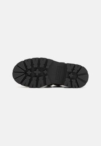 Melnas gumijas zoles ar tampeišu, fakturētu zīmējumu, kas nodrošina saķeri. Centrā ir "STEVE MADDEN" zīmols.