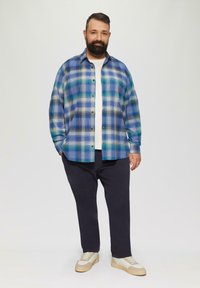 Geverfde flanellen shirt in blauw, groen en wit, met een knoopsluiting aan de voorkant. Gecombineerd met donkere broek en lichte sneakers.
