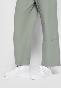 Bílé tenisky s hladkým koženým povrchem a perforovanými detaily, spárované s volnými, světle zelenými kalhotami střední délky.