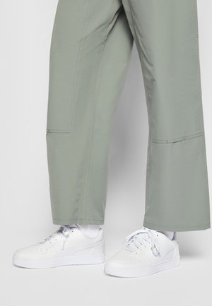 Vita sneakers med slät läderstruktur och perforerade detaljer, kombinerade med löst sittande, ljusgröna, midjelånga byxor.