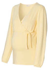 Geel wikkelshirt met lange mouwen en een zijstrikdetail. Gemaakt van zachte stof, met een diepe V-halslijn en gathers bij de manchetten. Geschikt voor zwangerschapskleding.