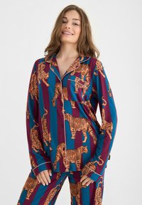 Ensemble de pyjama avec un imprimé tigre orange, présentant des rayures teal et bordeaux. Tissu doux, manches longues et fermeture à boutons devant.