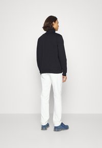 Hanorac negru cu guler înalt, pantaloni albi și adidași albaștri. Material neted, croială relaxată și design minimalistic.