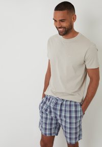 Camiseta corta de manga corta en color beige claro combinada con shorts de baño a cuadros en azul y blanco, con cinturilla elástica y cordón blanco.