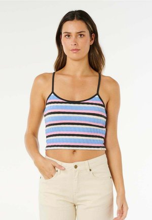 Femme portant un crop top rayé sans manches aux couleurs bleu, rose, noir et blanc, assorti à un pantalon beige taille haute.