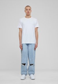 Camiseta de algodón blanca, de corte relajado; jeans descoloridos azul claro con grandes desgastes; zapatillas blancas; diseño simple y sin adornos.