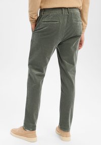 Zielone spodnie sztruksowe o fakturowanej powierzchni, z elastycznym paskiem w talii, kieszeniami bocznymi i tylnymi oraz dopasowanym krojem. W połączeniu z beżowym obuwiem.