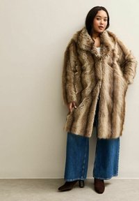 Faux-Fur-Mantel in Braun- und Beigetönen, mit weitem Kragen und lockerer Passform. Kombiniert mit blauen weit geschnittenen Jeans und braunen Stiefeletten mit Absatz.