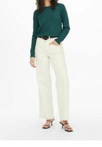 Maglione verde lavorato a maglia, jeans color crema a vita alta con una vestibilit�à ampia e tacchi neri con cinturino alla caviglia. Abbigliamento accentuato da una cintura nera.