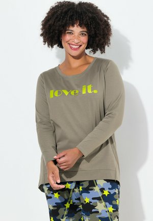 T-shirt à manches longues vert olive avec le texte "love it." en jaune vif. Associé à un pantalon coloré à motif camouflage avec des étoiles.