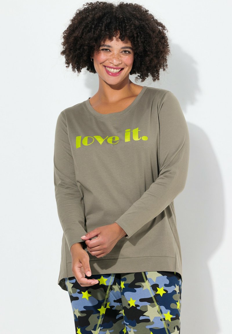 Olivgrünes Langarm-T-Shirt mit dem Text "love it." in leuchtendem Gelb. Kombiniert mit bunten Camo-Print-Hosen mit Sternen.