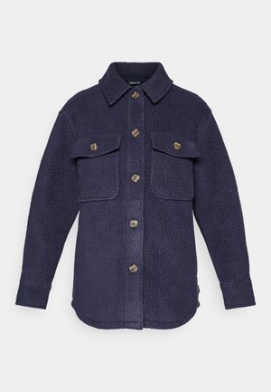 Marineblå fleece skjortejakke med to brystlommer, knappelukking og teksturert stoff. Har krage og synlige sømaksenter.