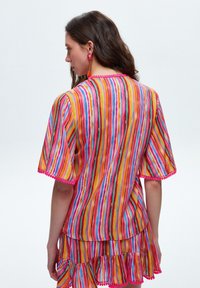 Multifarvet stribet bluse med korte ærmer og fl�æset kant. Har pink hæklede detaljer og en let, svævende stofstruktur.