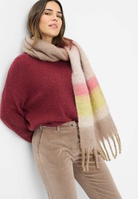 Lichtgewicht gebreide sjaal in beige met roze en gele strepen, met franjes aan de randen. Draagt met een kastanjebruwe trui en beige corduroy broek.