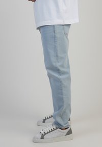 Jeans de mezclilla azul claro con corte recto, combinados con zapatillas blancas y grises con un diseño texturizado y acentos en contraste.