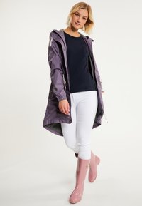 Violetinis nepralaidus vandeniui švarkas su gobtuvu, elastingomis rankovėmis, derinamas su tamsiai mėlynu marškinėliu, baltais kelnais ir blizgiais rožiniais lietaus batais. Sklandus paviršius, praktiškas dizainas.