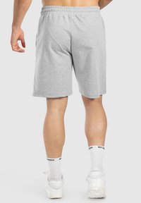 Pantalones cortos de algodón grises con una cinturilla elástica, corte a la altura de la rodilla y bolsillos laterales, combinados con calcetines blancos y zapatillas.
