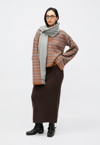 Pull rayé marron et gris avec un col montant, associé à une longue jupe marron. Une écharpe grise est posée négligemment, et des bottes noires complètent la tenue.